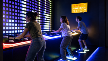 Three people playing interactive arcade games at Power Play Sydney.