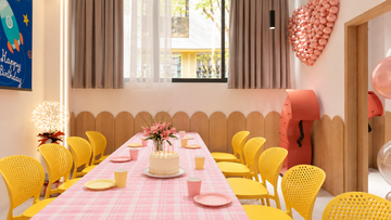 Birthday party room with a pink table setting, yellow chairs and a cake at Power Play Sydney.
